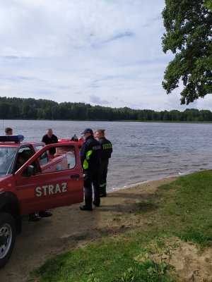 Policjant i strażacy stoją nad brzegiem jeziora